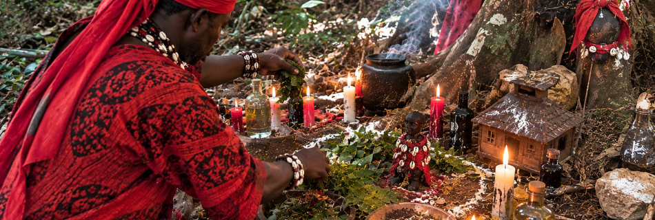 Marabout réalisant un rituel africain de protection spirituelle d'une maison dans une forêt, avec des plantes, des cauris et des bougies.